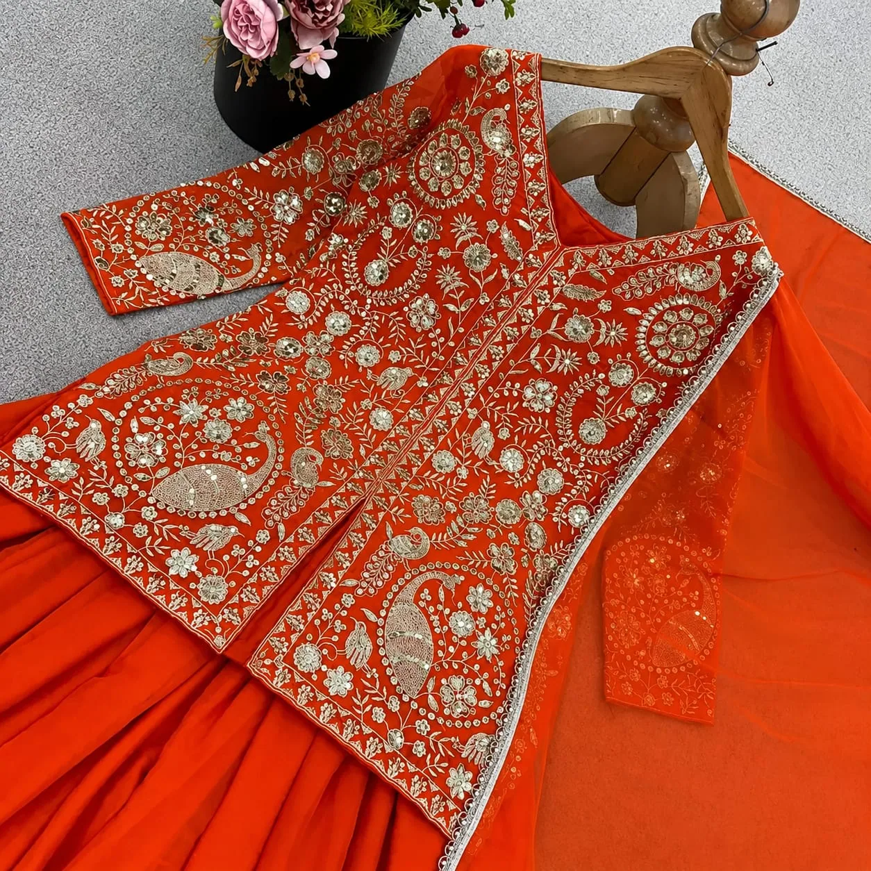 The orange kurta on a hanger, showing the sequinned peacock embroidery up close